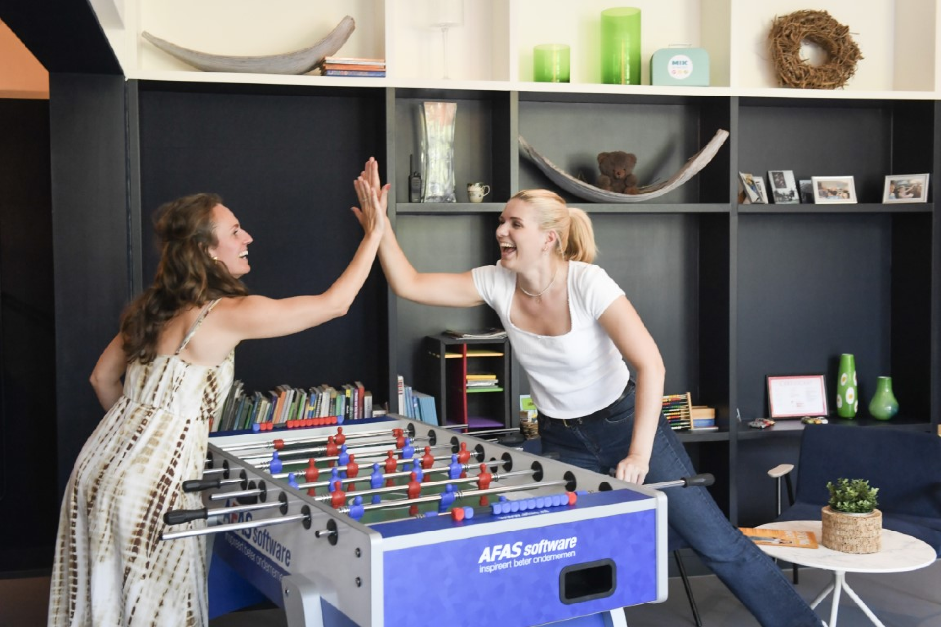 High five door twee lachende collega's bij een tafelvoetbalspel.