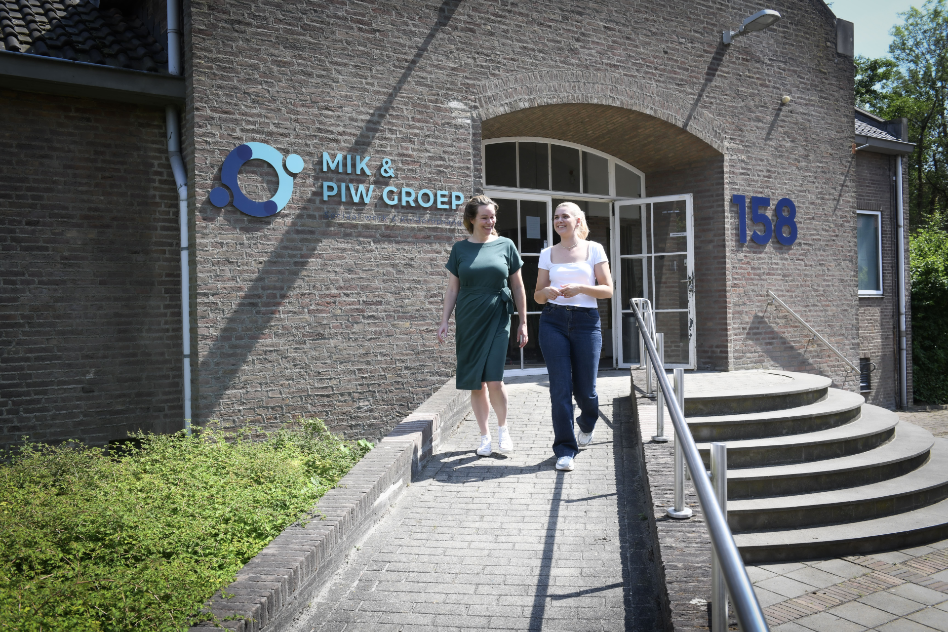Twee collega's lopen gezellig kletsend naar buiten bij het kantoor van MIK & PIW Groep.